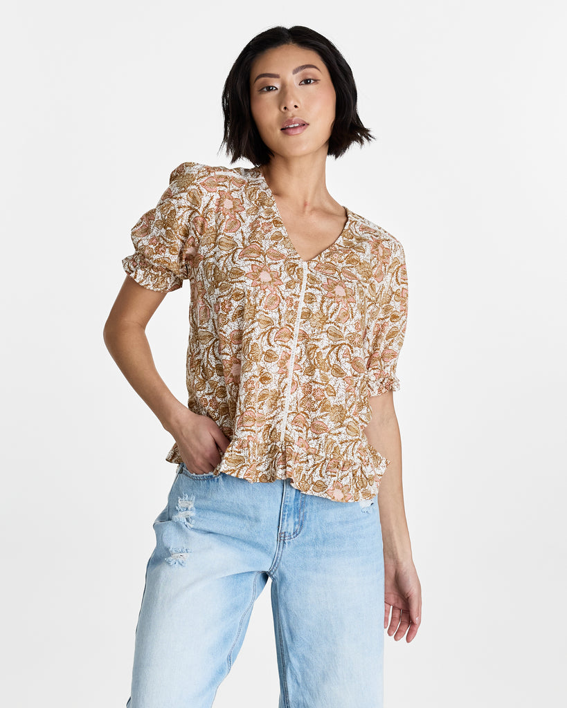 Woman in a tan floral print, short sleeve, v-neck blouse