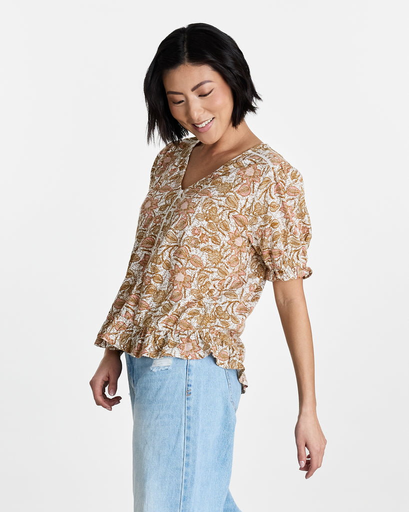 Woman in a tan floral print, short sleeve, v-neck blouse