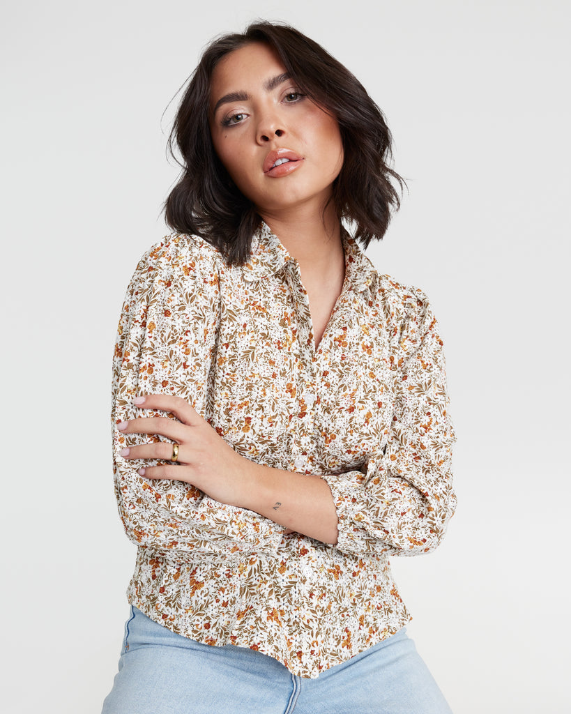 Woman in a tan floral print, 3/4 sleeve, buttondown blouse