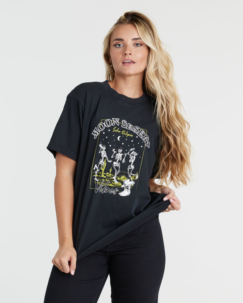 Woman in a black short sleeve graphic t-shirt with "Moon Desert" writtin on the front