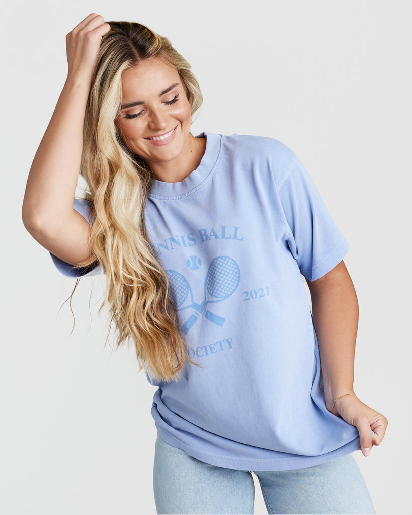 Woman in a blue short sleeve graphic t-shirt with tennis rackets on front