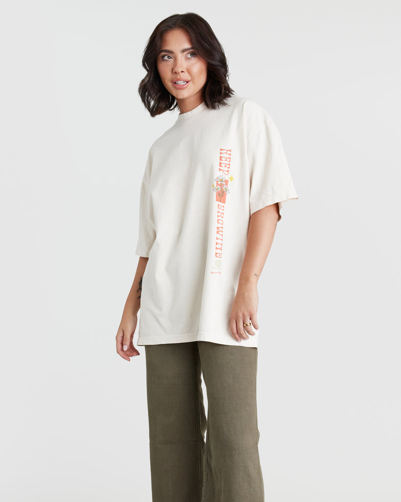 Woman in a cream, oversized graphic t-shirt that reads "Life Is Good" on the back and "keep growing" on the front