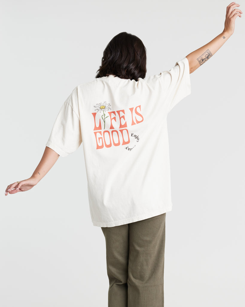 Woman in a cream, oversized graphic t-shirt that reads "Life Is Good" on the back and "keep growing" on the front