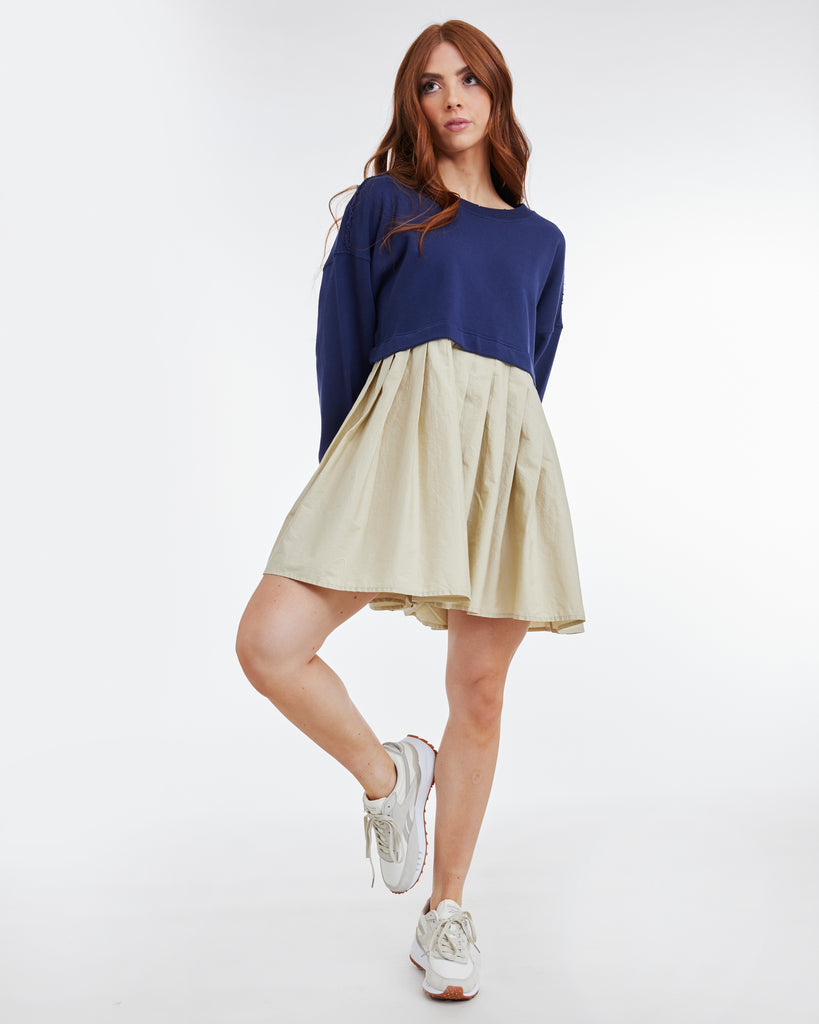 Woman in a tan and blue colorblocked mini dress with long sleeves.