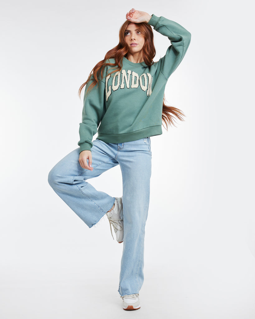 Woman in a green long sleeve sweatshirt with "LONDON" across the front
