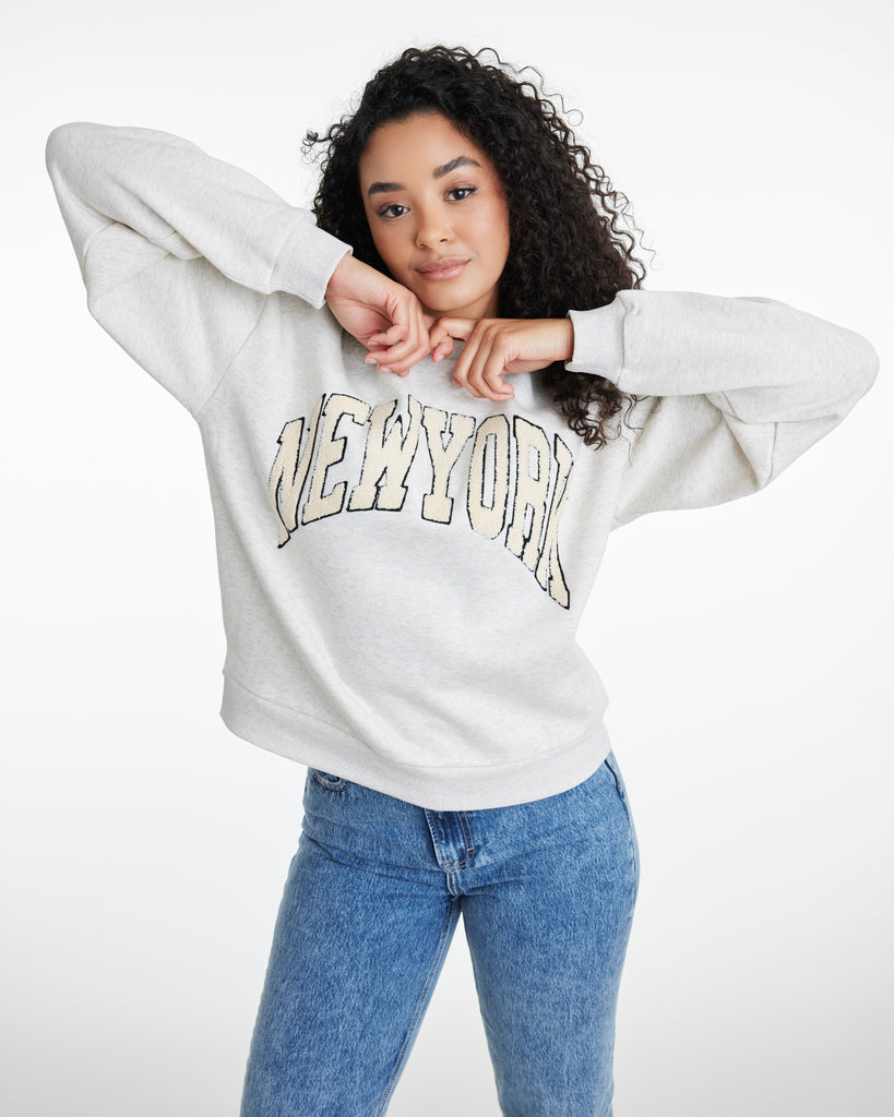Woman in a gray long sleeve sweatshirt with "NEW YORK" across the front